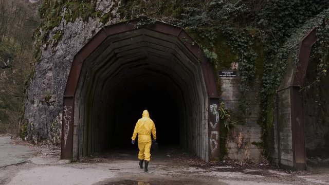 Rear view, a Man in a yellow protective suit with a suitcase goes to the tunnel in the mountain. Wide Shot