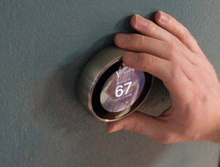 Hand adjusting the dial on smart home thermostat. Pressing center button to save money heating and cooling.