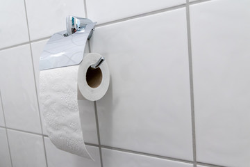 Halbe Rolle weißes Klopapier auf Metall-Klorollenhalter im Badezimmer und weißen Fliesen der Toilette zeigt Corona-Krise in Deutschland