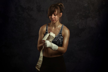 Obraz na płótnie Canvas Woman ready for fight concept. Boxer fighter girl in sports top, wraps his hands elastic bandages fists on black