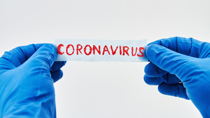 Hands in blue medical gloves are holding inscription Coronavirus on white background.