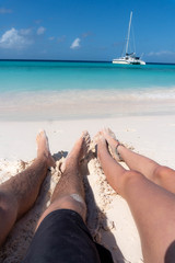 Legs of a young couple on a white sandy beach with a turquoise blue ocean.