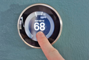 Hand adjusting the dial on nest smart home thermostat. Pressing center button to save money heating and cooling.