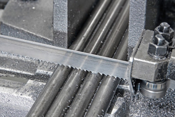 automatic band saw with coolant liquid cuts the metal rods of the workpiece
