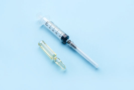 Medical ampoule with the drug and a disposable syringe on a blue background. Medicine infectious concept. Copy space for text.