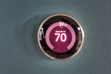 Nest smart home thermostat with red center information on blue wall. Heating home temperature to 70 degrees.