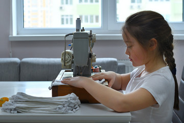 Young woman making home made breathing mask, corona virus protection.Homemade medical mask in the process. Sewing virus face mask at home. Detail on sewing machine.