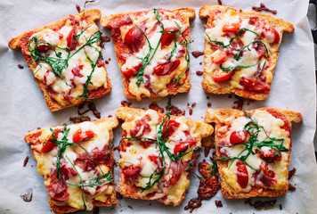 Hot pizza toasts with sausage, cheese, cherry tomatoes and arugula close-up - obrazy, fototapety, plakaty