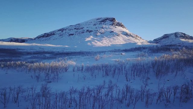 Aerial sunny winter view of Abisko National Park, Kiruna Municipality, Lapland, Norrbotten County, Sweden, shot from drone, with road and mountains