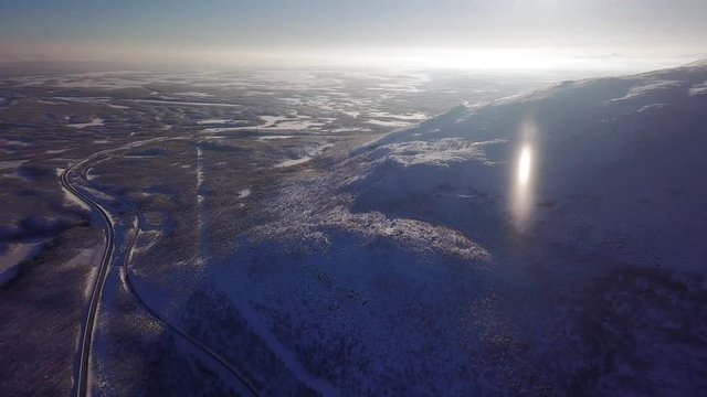Aerial sunny winter view of Abisko National Park, Kiruna Municipality, Lapland, Norrbotten County, Sweden, shot from drone, with road and mountains