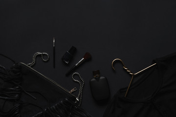 Black monochromatic flatlay composition on black background. Hangers, make-up brush, handbag, sunglasses, perfume, phone,nail polish, belt.Minimalist black, black friday.Top view, Copy Space Flat Lay.