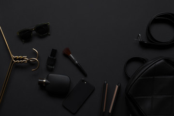 Black monochromatic flatlay composition on black background. Hangers, make-up brush, handbag, sunglasses, perfume, phone,nail polish, belt.Minimalist black, black friday.Top view, Copy Space Flat Lay.