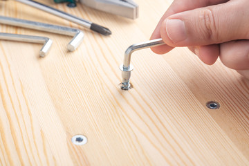 The furniture assembler tightens the cam bolt fixing into the furniture made of particle board with...