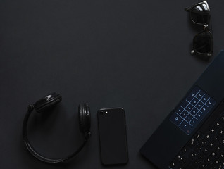 Laptop, phone,  watch,  sunglasses over monochrome black  background. Work accessories of a blogger with copy space and top view. Minimalist black  trendy, Flat Lay