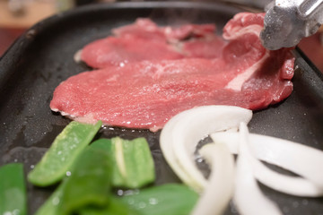 トングで肉をホットプレートに置いて焼く