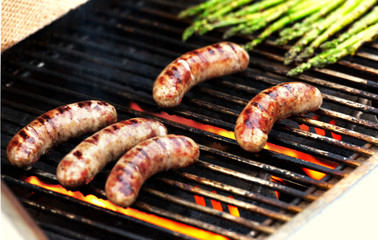 Bratwurst and asparagus cooking on a grill.