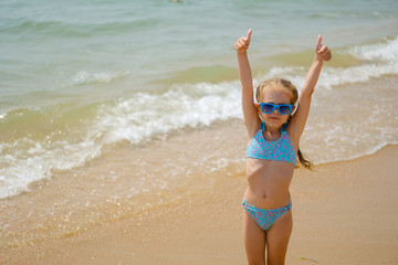 Child in sunglasses on the ocean. Little girl on the beach.