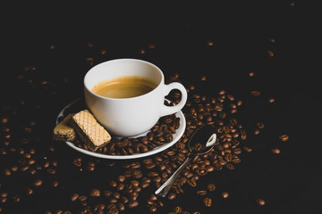 cup of coffee with beans on black background and cracker