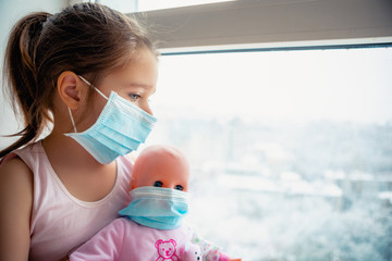 Little girl with doll wearing a protective mask. Copy space. Sadness kid at home in isolation. Sick...
