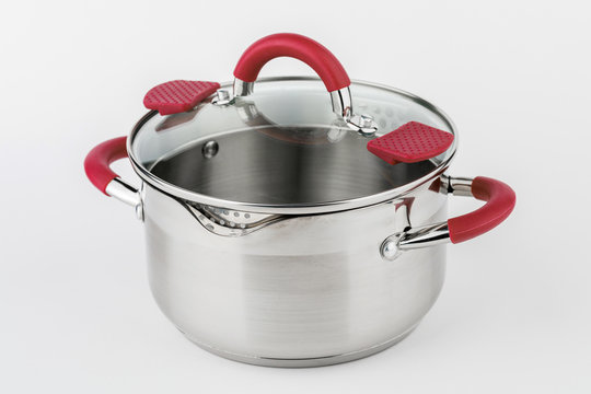 Stainless casserole with glass lid and red handles on grey background.