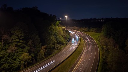 Long exposure time lapse of light trails headlights and tail lights from traffic on a curved highway road leading towards downtown Toronto at night with trees lining the sides of the road.