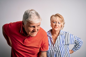 Senior beautiful couple standing together over isolated white background Suffering of backache, touching back with hand, muscular pain