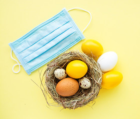 Easter colored eggs in the nest on yellow background with protective face mask - concept of...
