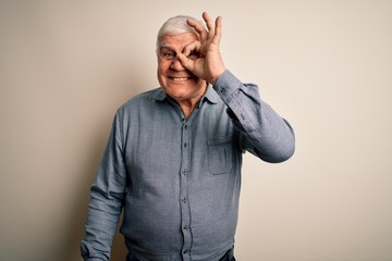 Senior handsome hoary man wearing casual shirt standing over isolated white background doing ok gesture with hand smiling, eye looking through fingers with happy face.