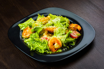 Caesar salad with prawns on a black plate on brown wooden table