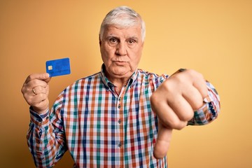 Senior handsome hoary customer man holding credit card to finance payment with angry face, negative sign showing dislike with thumbs down, rejection concept