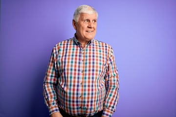 Fototapeta premium Senior handsome hoary man wearing casual colorful shirt over isolated purple background looking away to side with smile on face, natural expression. Laughing confident.