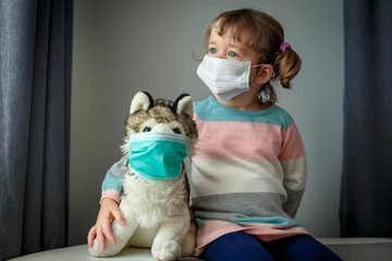 Quarantine at kindergarten. Toddler girl and her dog toy with protection masks. Coronavirus...