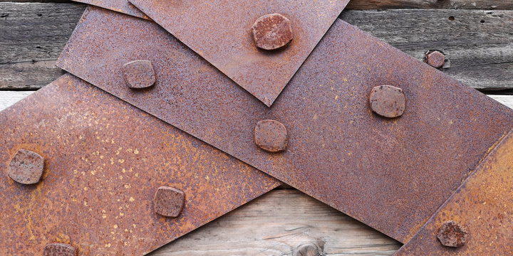 Closeup texture of rusty iron sheets or slats bolted to aged wooden planks in grayish-brown tones with yellow flecks. Concept of banning,prohibition or closing anything.Brutal wallpaper or background