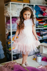 Little girl in a pink dress posing on a table in a sewing atelier
