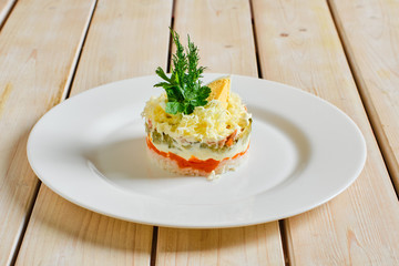 Layered salad with rice, carrot, pickled cucumber, pulled beef and cheese on wooden table