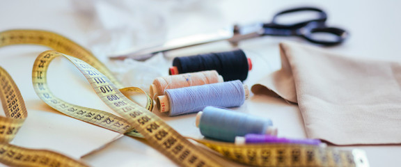 Composition of seamstress threads and scissors on a white table. Concept of a clothing designer - obrazy, fototapety, plakaty