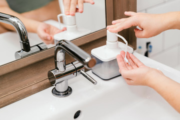 woman takes care of her hands in the bathroom with a special soap and moisturizer.