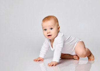 Chubby ginger little one in bodysuit, barefoot. He is sitting on floor isolated on white studio background. Close up, copy space