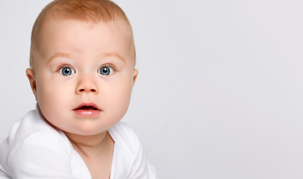 Portrait of a chubby red-haired baby in a bodysuit. He looks in surprise at the camera isolated on a white studio background.