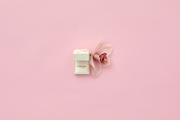 Pink box with engagement ring and orchid flower on pink background, top view. Space for text