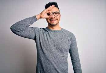 Young handsome man wearing casual sweater and glasses over isolated white background doing ok gesture with hand smiling, eye looking through fingers with happy face.