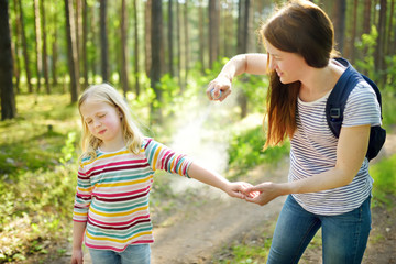 Mother applying insect repellent to her daughter before forest hike summer day. Protecting children from biting insects at summer. Using bug spray. Active leisure with kids.