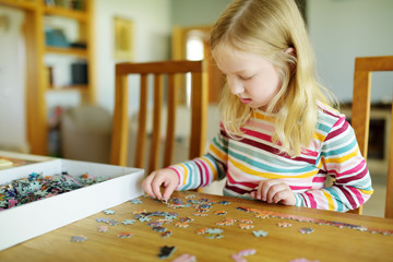 Cute young girl playing puzzles at home. Child connecting jigsaw puzzle pieces in a living room table. Kid assembling a jigsaw puzzle. Fun family leisure.