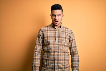 Young handsome man wearing casual shirt standing over isolated yellow background In shock face, looking skeptical and sarcastic, surprised with open mouth