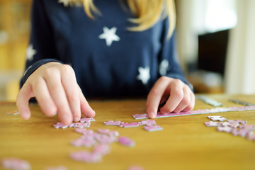 Close-up on child's hands playing puzzles at home. Child connecting jigsaw puzzle pieces in a living room table. Kid assembling a jigsaw puzzle. Stay at home activity for kids.