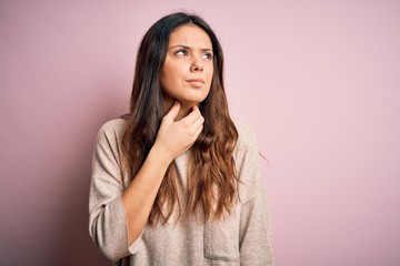 Young beautiful brunette woman wearing casual sweater standing over pink background Touching painful neck, sore throat for flu, clod and infection