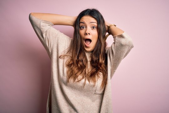 Young beautiful brunette woman wearing casual sweater standing over pink background Crazy and scared with hands on head, afraid and surprised of shock with open mouth