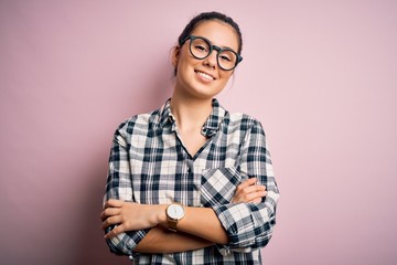 Young beautiful brunette woman wearing casual shirt and glasses over pink background happy face smiling with crossed arms looking at the camera. Positive person.