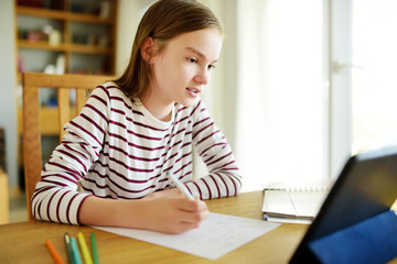 Smart preteen schoolgirl doing her homework with digital tablet at home. Education and distance...