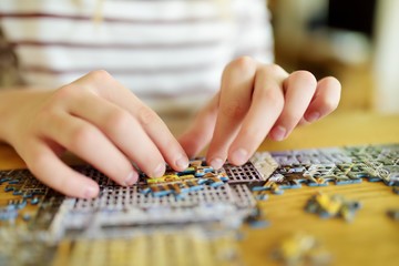 Fototapeta premium Close-up on child's hands playing puzzles at home. Child connecting jigsaw puzzle pieces in a living room table. Kid assembling a jigsaw puzzle. Stay at home activity for kids.